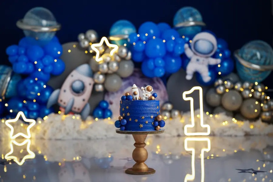 Escenario espacial con globos azules, cohete, astronauta y un pastel azul
