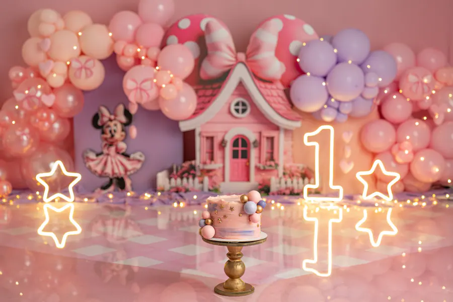 Escenario de smash cake rosado con casita, globos, luces y un pastel sobre una base dorada